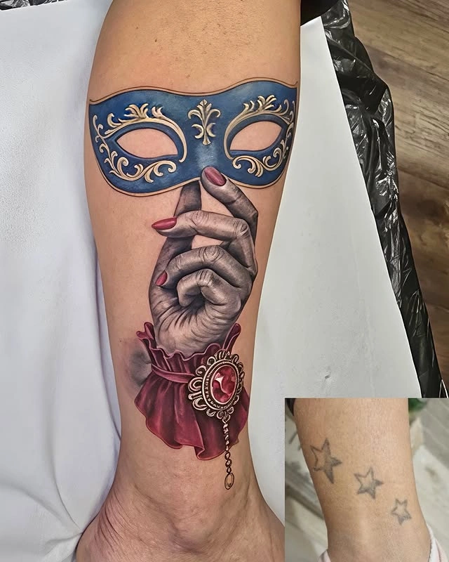 Tatuaj detaliat cu o mână ținând o mască albastră decorată.