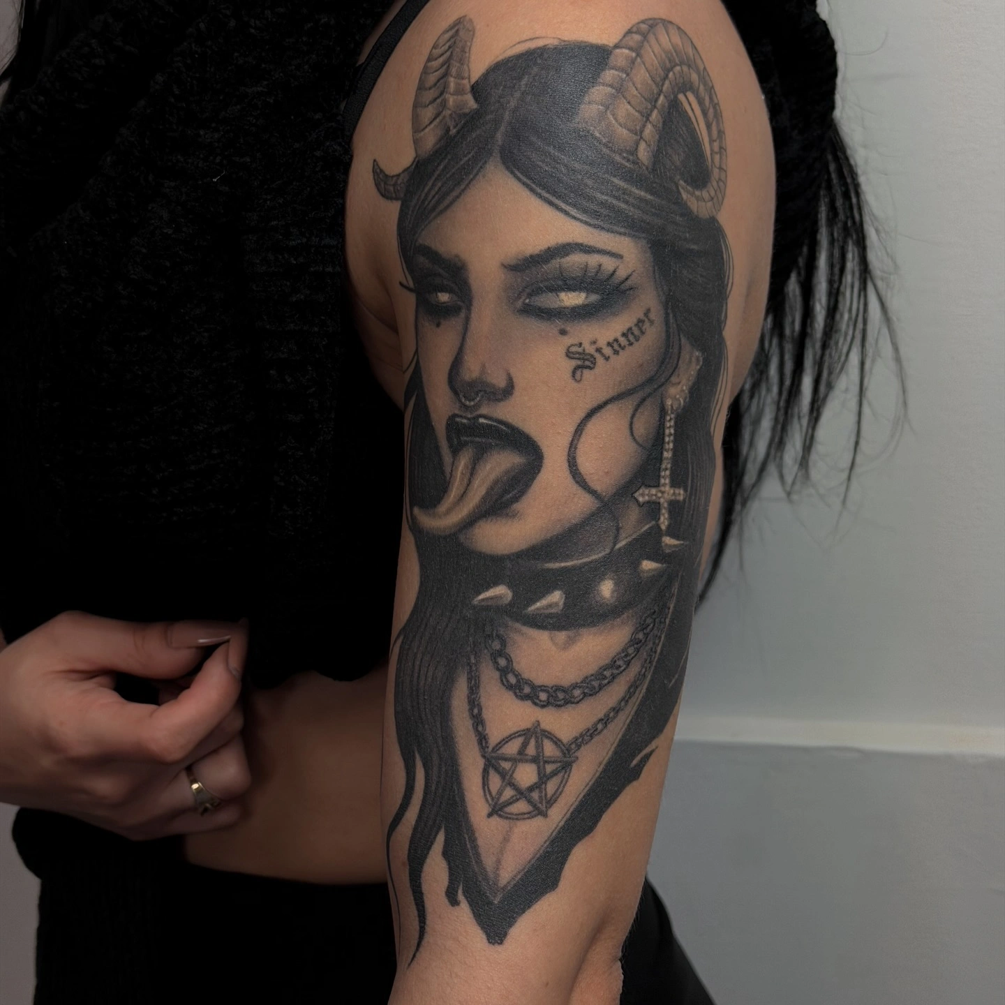 Tatuaj pe braț reprezentând un demon feminin cu coarne, limba scoasă și pentagramă