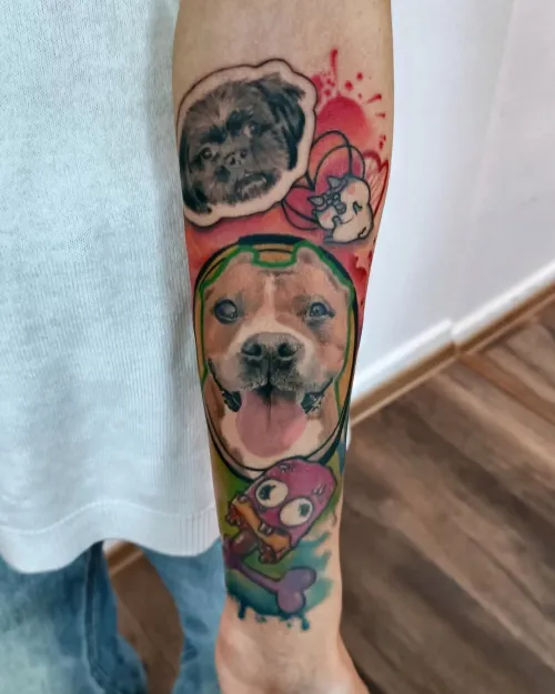 Tatuaj mare pe antebraț cu portrete de câini, unul realist central și unul alb-negru sus, completate de elemente cartoon colorate și pete de culoare.