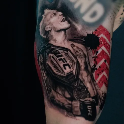 Tatuaj realist pe braț cu un luptător UFC purtând centura de campion, mănuși negre și elemente grafice roșii pe fundal.