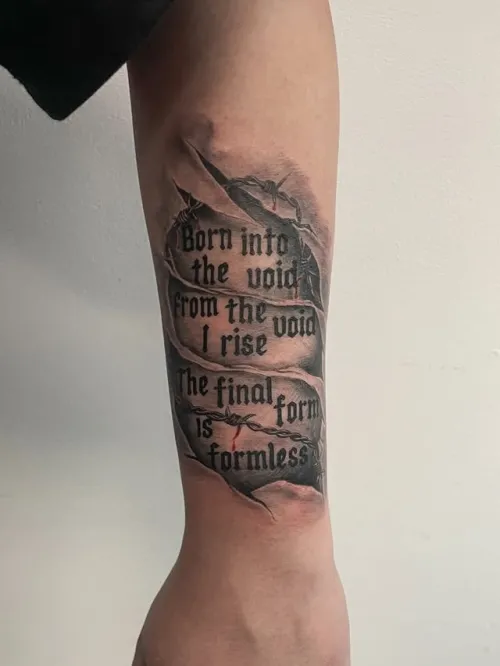 Tatuaj black and grey pe antebraț, cu text în font gotic și efect de piele ruptă, integrat cu umbre realiste și detalii de spini.