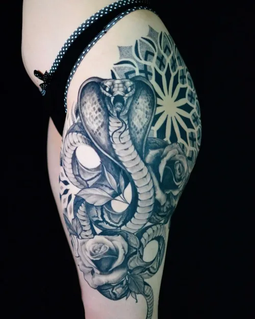 Tatuaj mare black and grey pe coapsă, cu o cobră realistă în prim-plan, trandafiri, frunze și elemente geometrice de tip mandala în fundal.